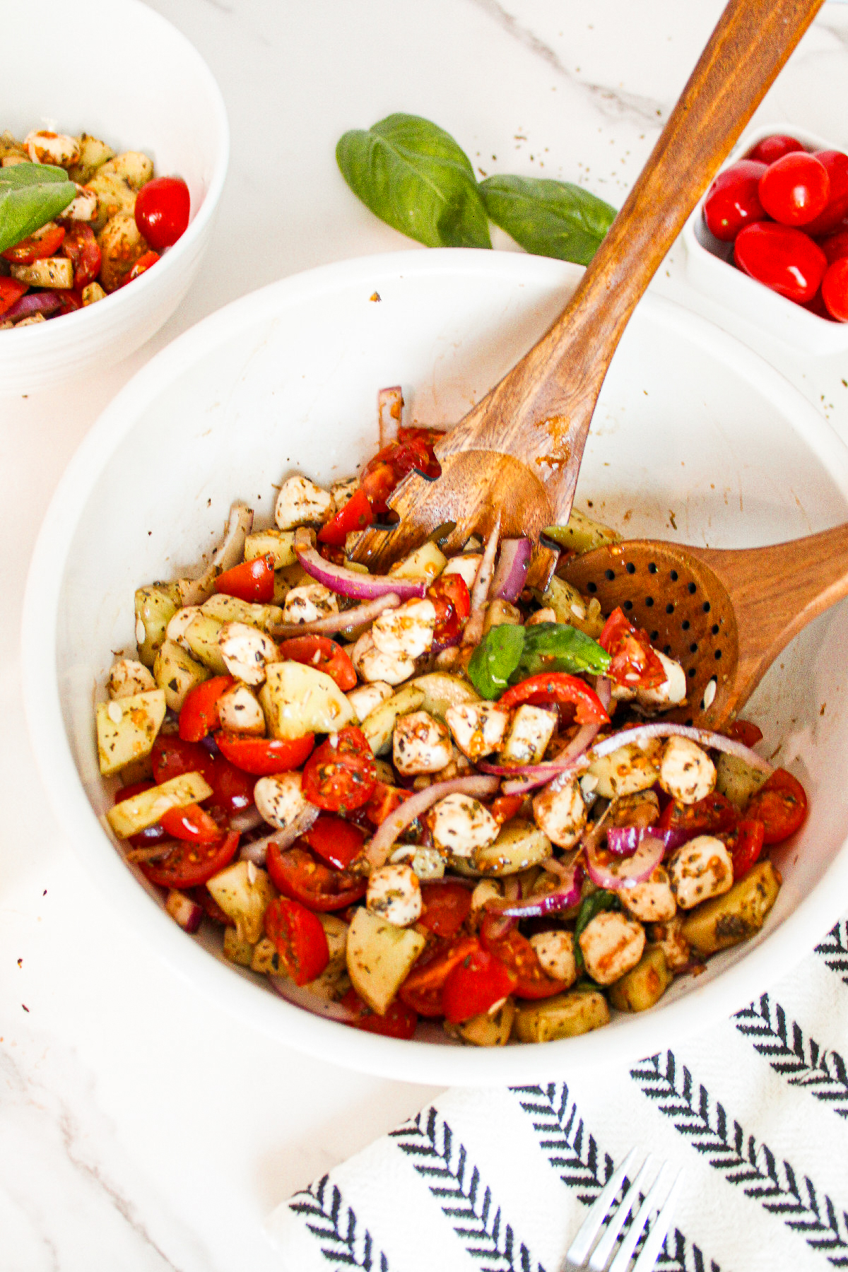 Wooden spoon adding rice vinegar herb dressing to cucumber caprese salad ingredients in a wooden mixing bowl before tossing.