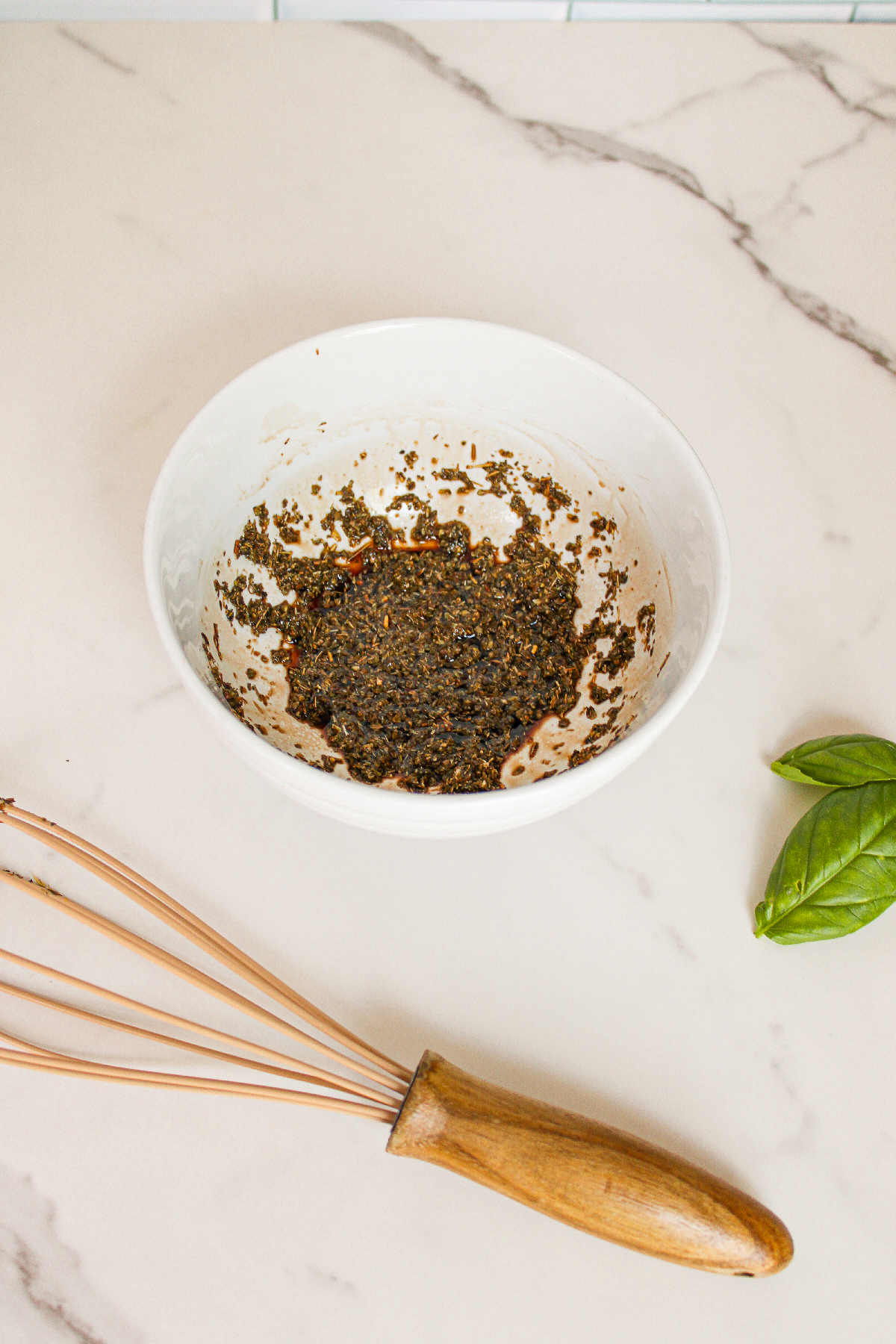 Dried oregano, olive oil, rice vinegar, salt, and pepper mixed together in a small bowl to make the dressing for cucumber caprese salad.