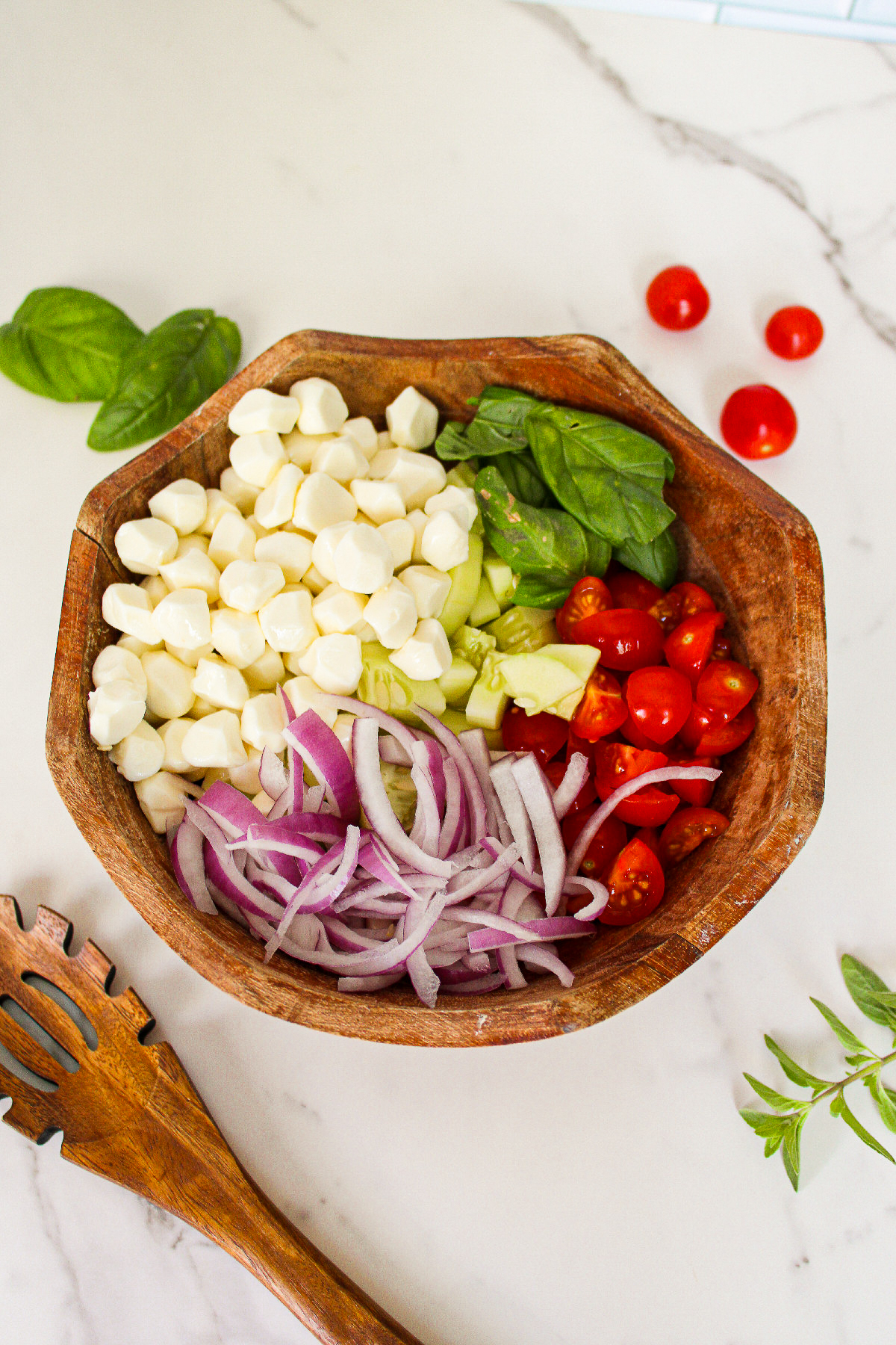 Chopped cucumber, cherry tomatoes, red onion, vegan mozzarella, and fresh basil combined in a wooden bowl before adding the dressing.