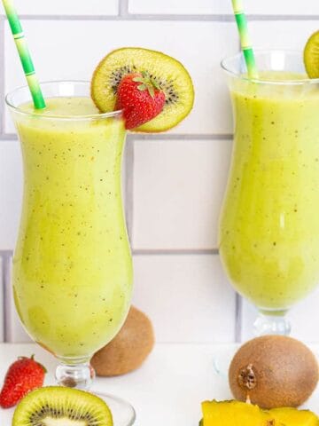 Two glasses of kiwi smoothies topped with fresh strawberries.