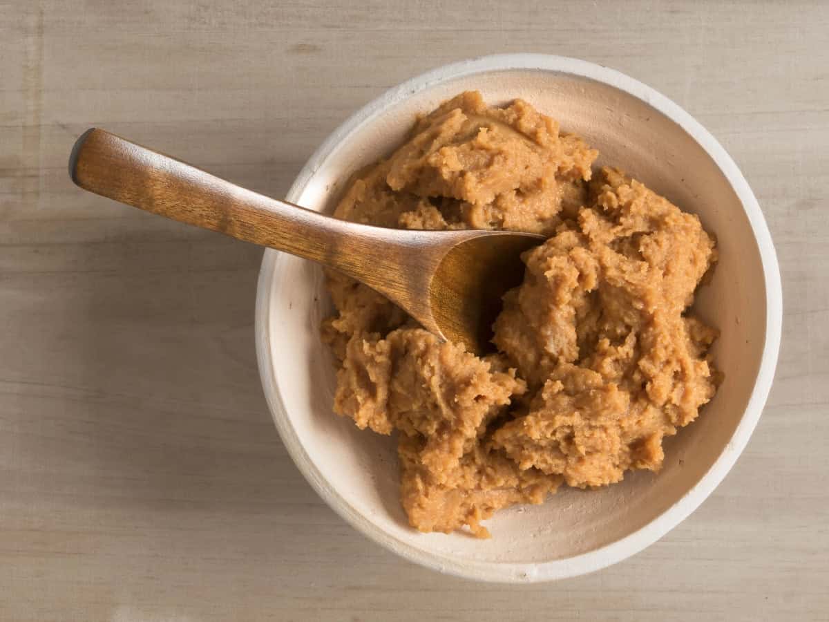 Top-down view of miso paste in a bowl with a wooden spoon on a light surface.