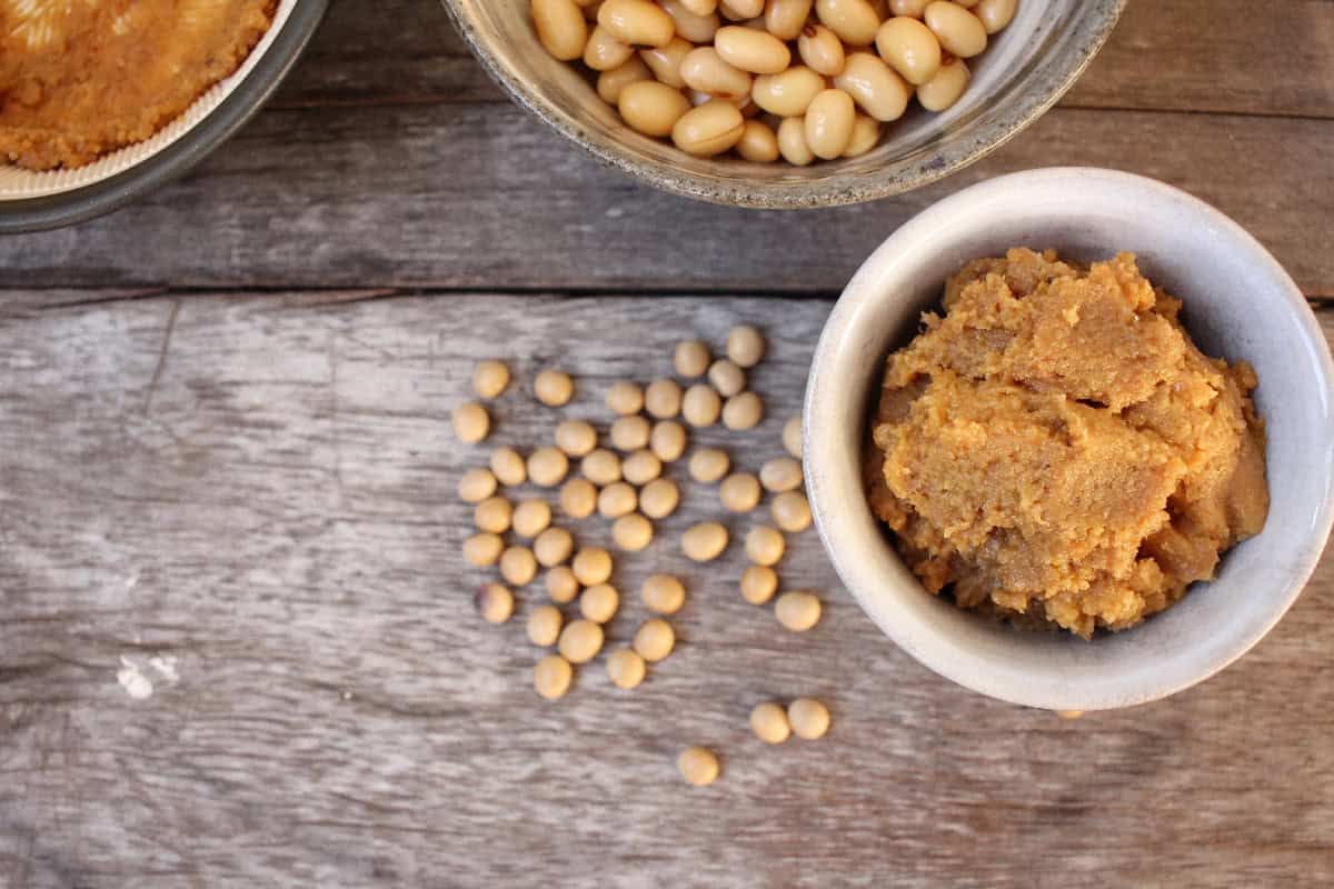 Miso paste in a small bowl with soybeans scattered on a rustic wooden table.