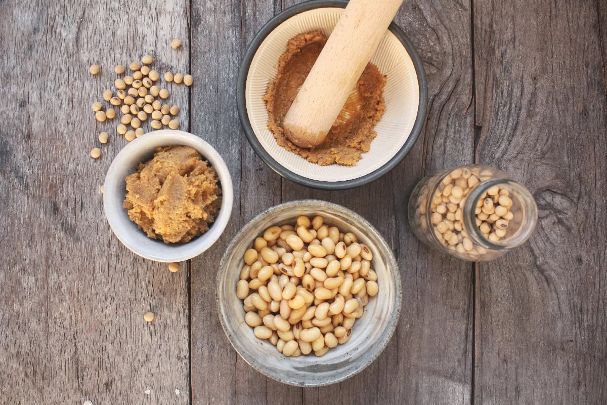 Miso paste and whole soybeans arranged in bowls on a wooden surface.
