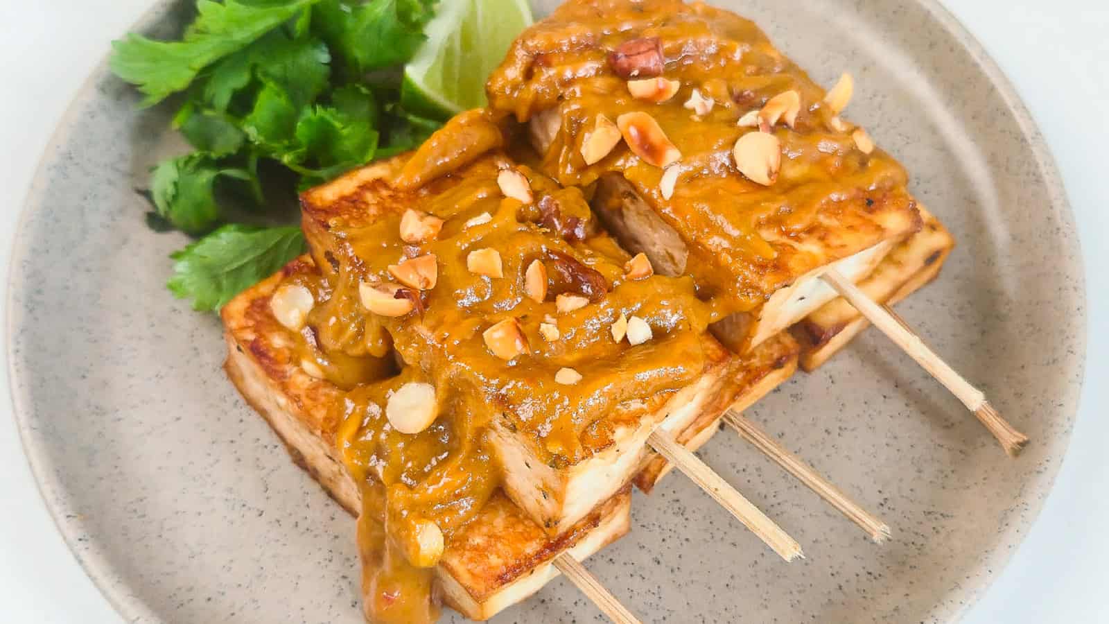Peanut satay tofu skewers drizzled with peanut sauce and topped with chopped peanuts.