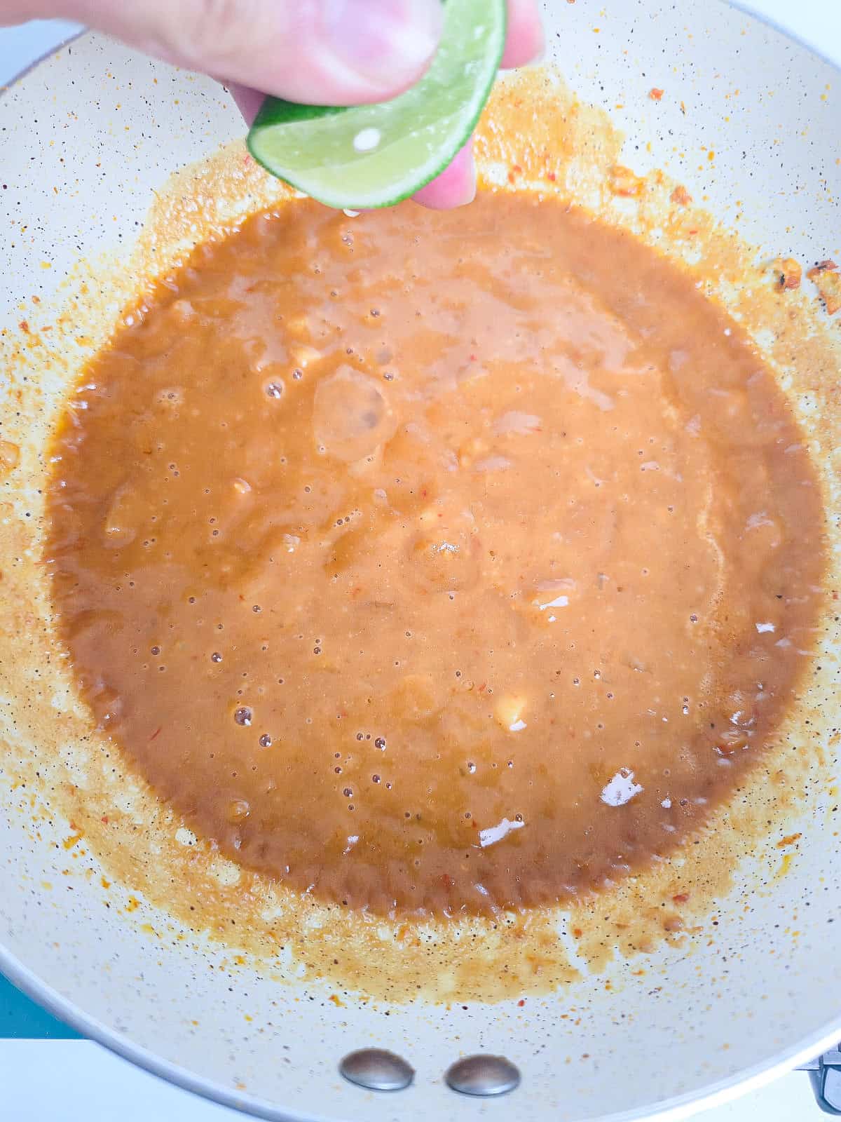 Fresh lime juice is squeezed into creamy peanut satay sauce in a skillet.