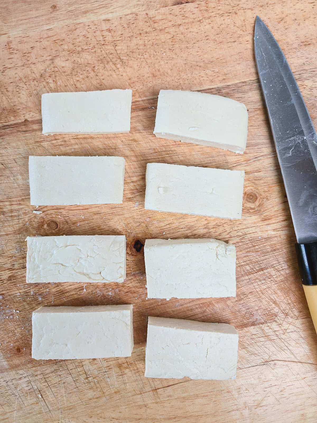 Firm tofu cut into thick rectangular pieces on a wooden cutting board.