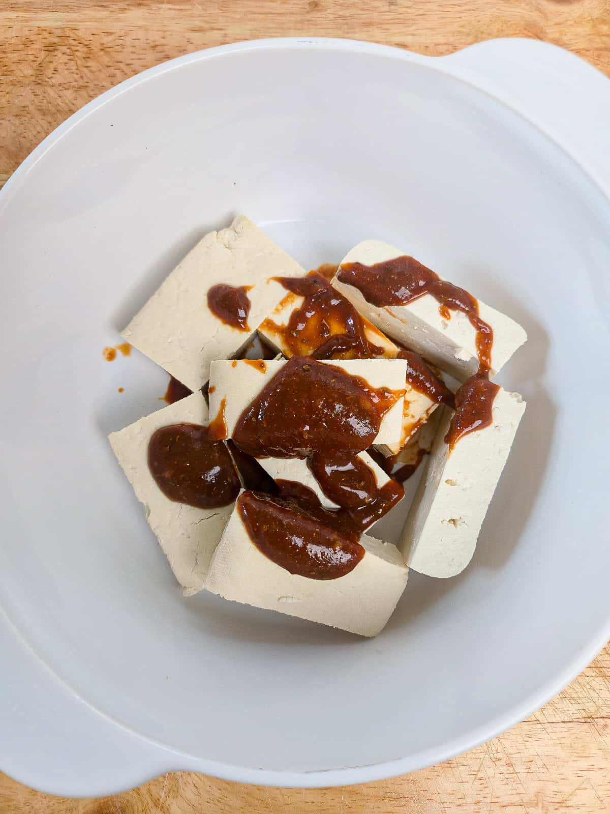 Tofu pieces topped with peanut satay marinade in a white mixing bowl.