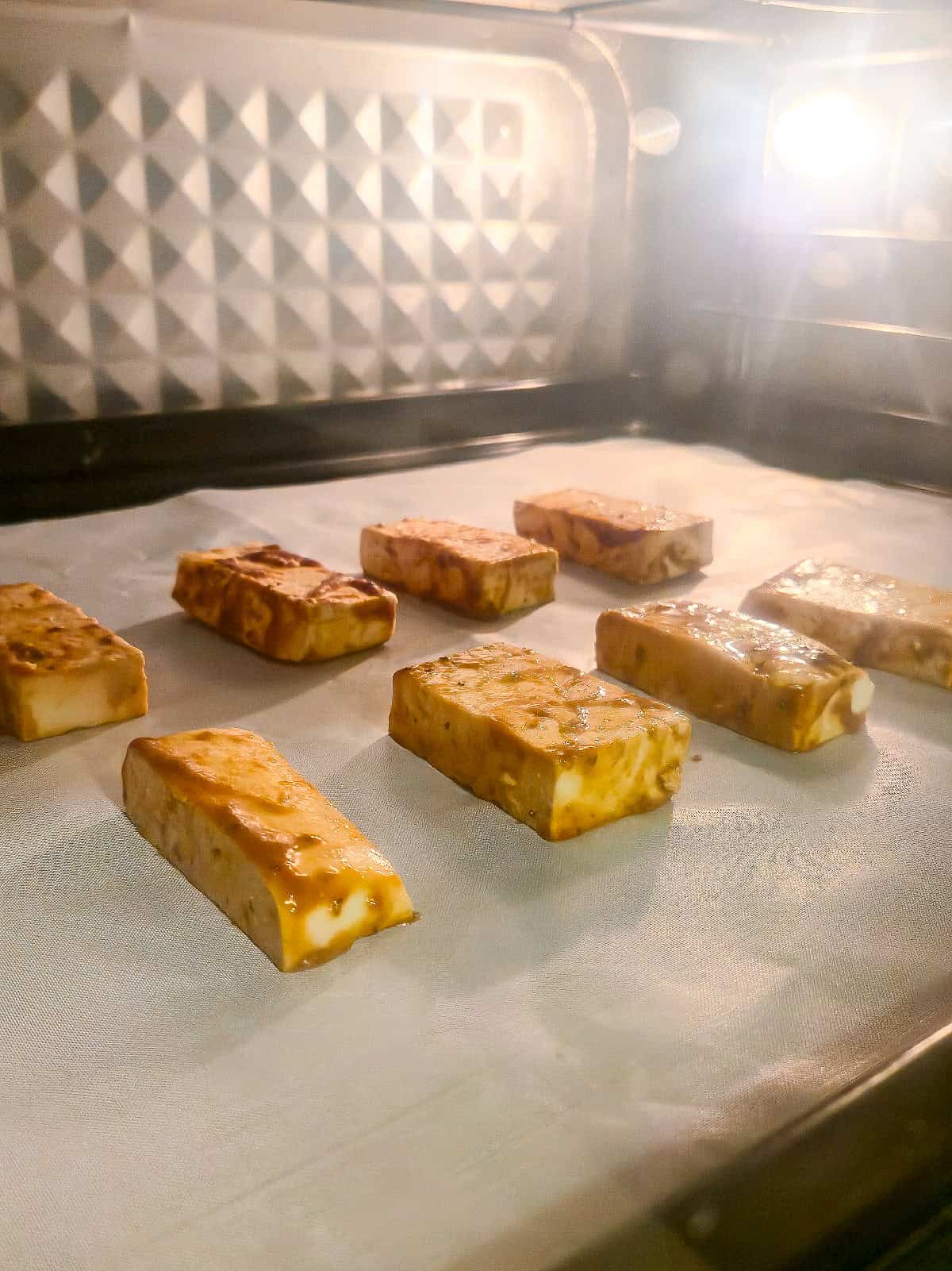Marinated tofu baking in the oven on a parchment-lined baking tray.