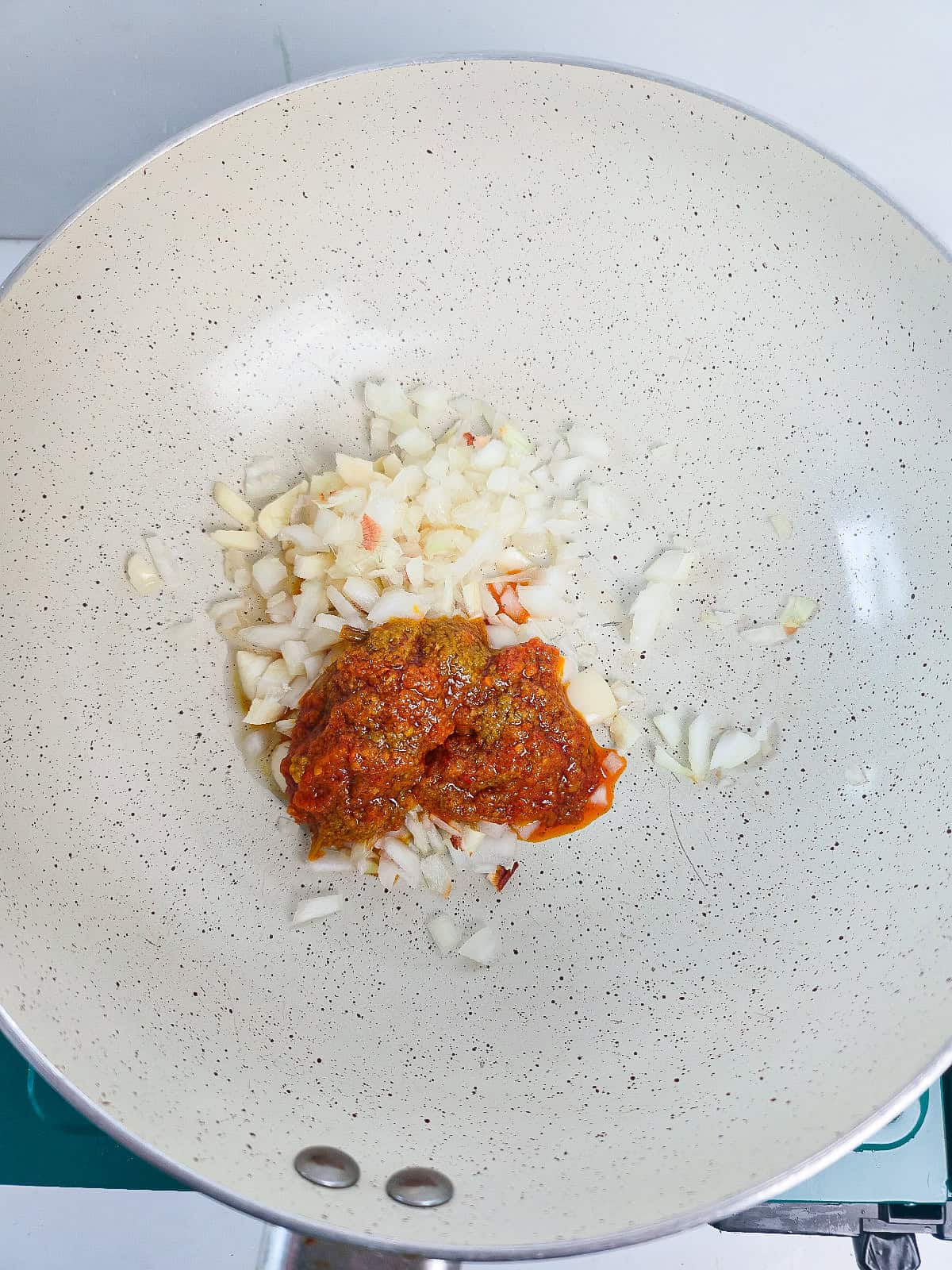 Diced onions, garlic, and red curry paste cooking in a skillet for satay sauce.