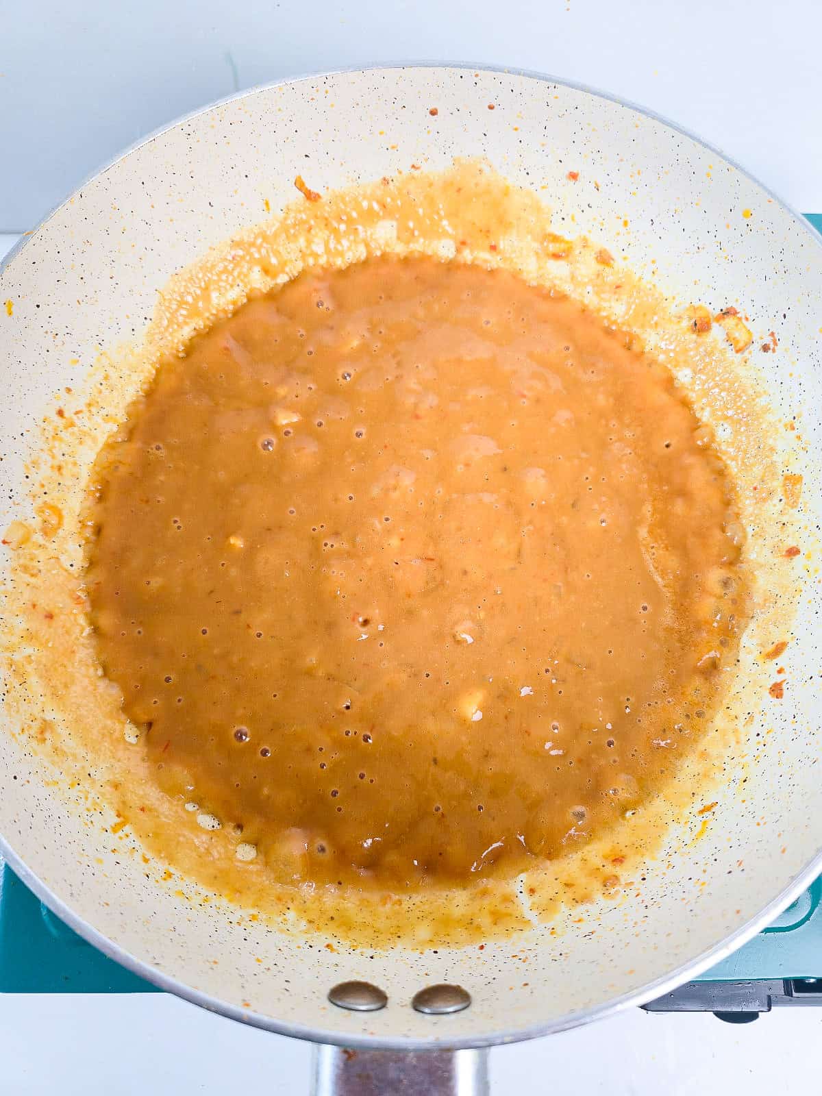 Creamy peanut satay sauce simmering in a skillet until smooth and bubbly.