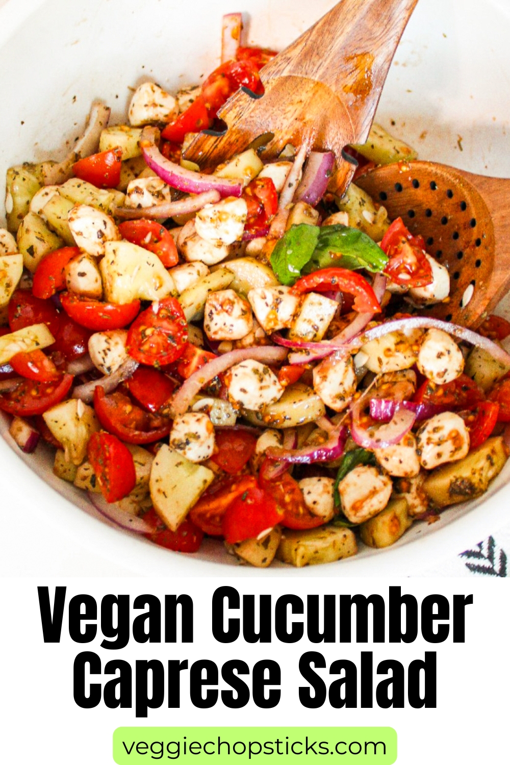 Cucumber caprese salad tossed with cherry tomatoes, vegan mozzarella pearls, red onion, fresh basil, and herb dressing in a serving bowl.