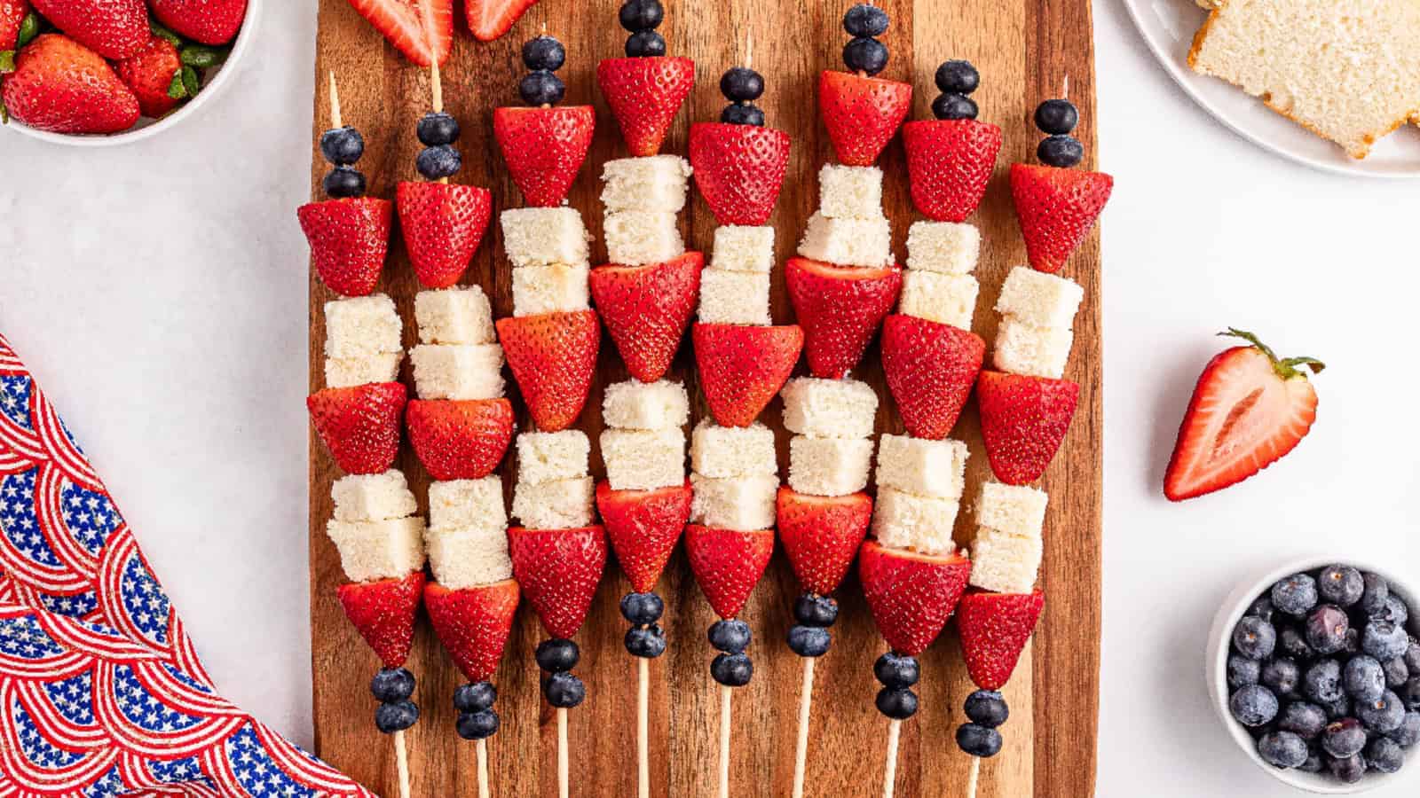 A wooden cutting board displaying assortment of strawberries pound cake pieces, and blueberries.