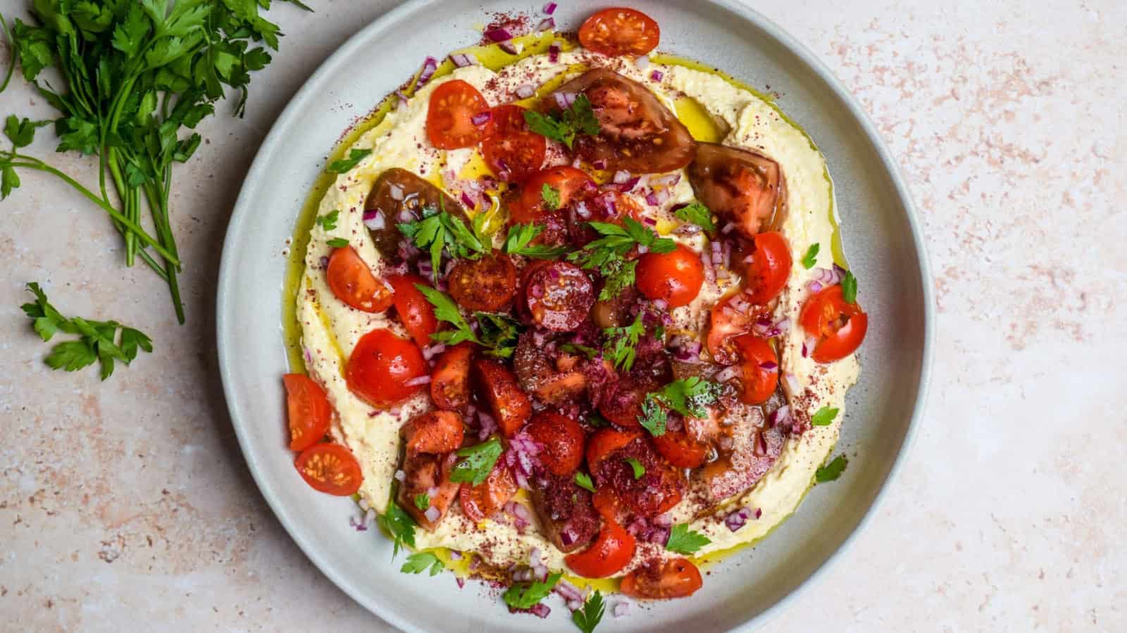 Tomato salad served with hummus and sprinkled with sumac seasoning.