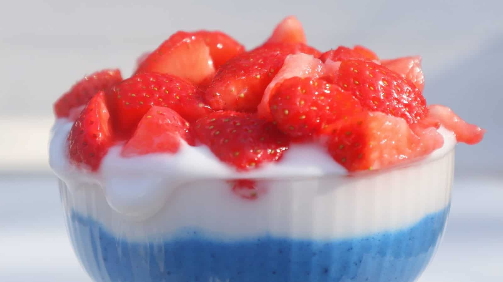 Coconut yogurt layered with colorful red and blue fruit toppings.
