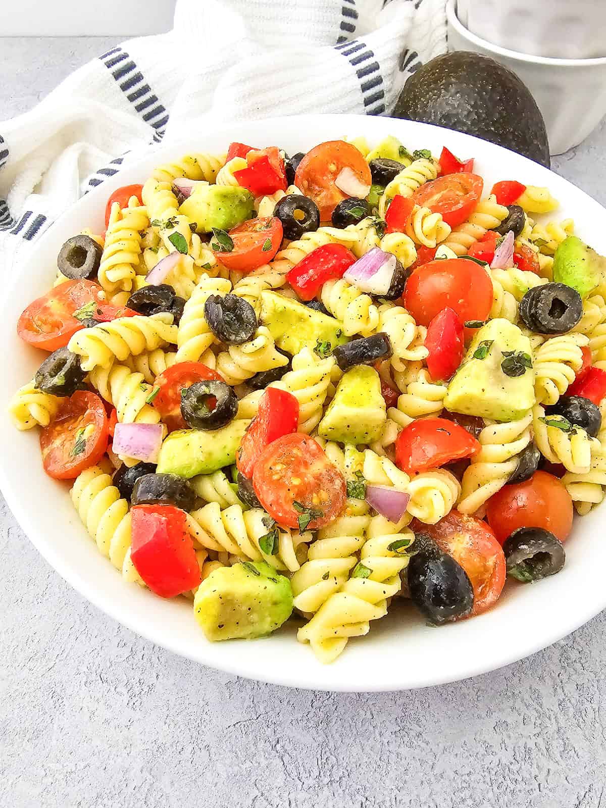 Close side view of vegan pasta salad highlighting avocado chunks, cherry tomatoes, black olives, and rotini pasta.
