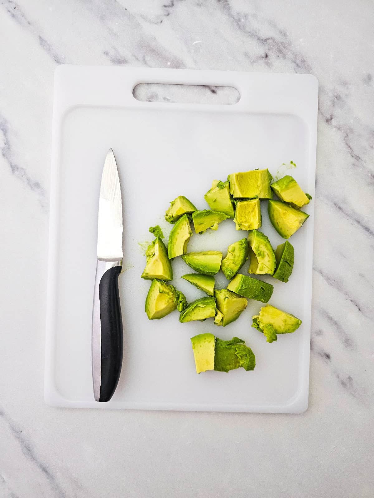 Diced avocado pieces on a white cutting board next to a small kitchen knife.