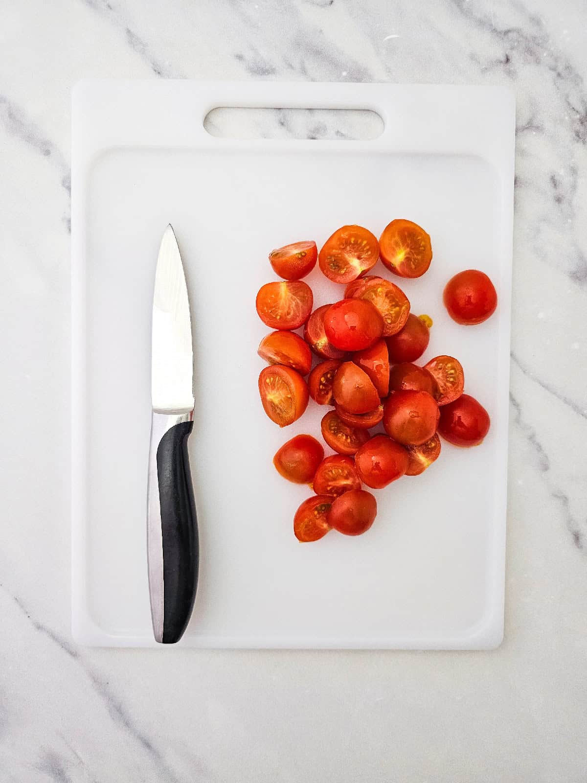 Halved cherry tomatoes on a white cutting board beside a kitchen knife.
