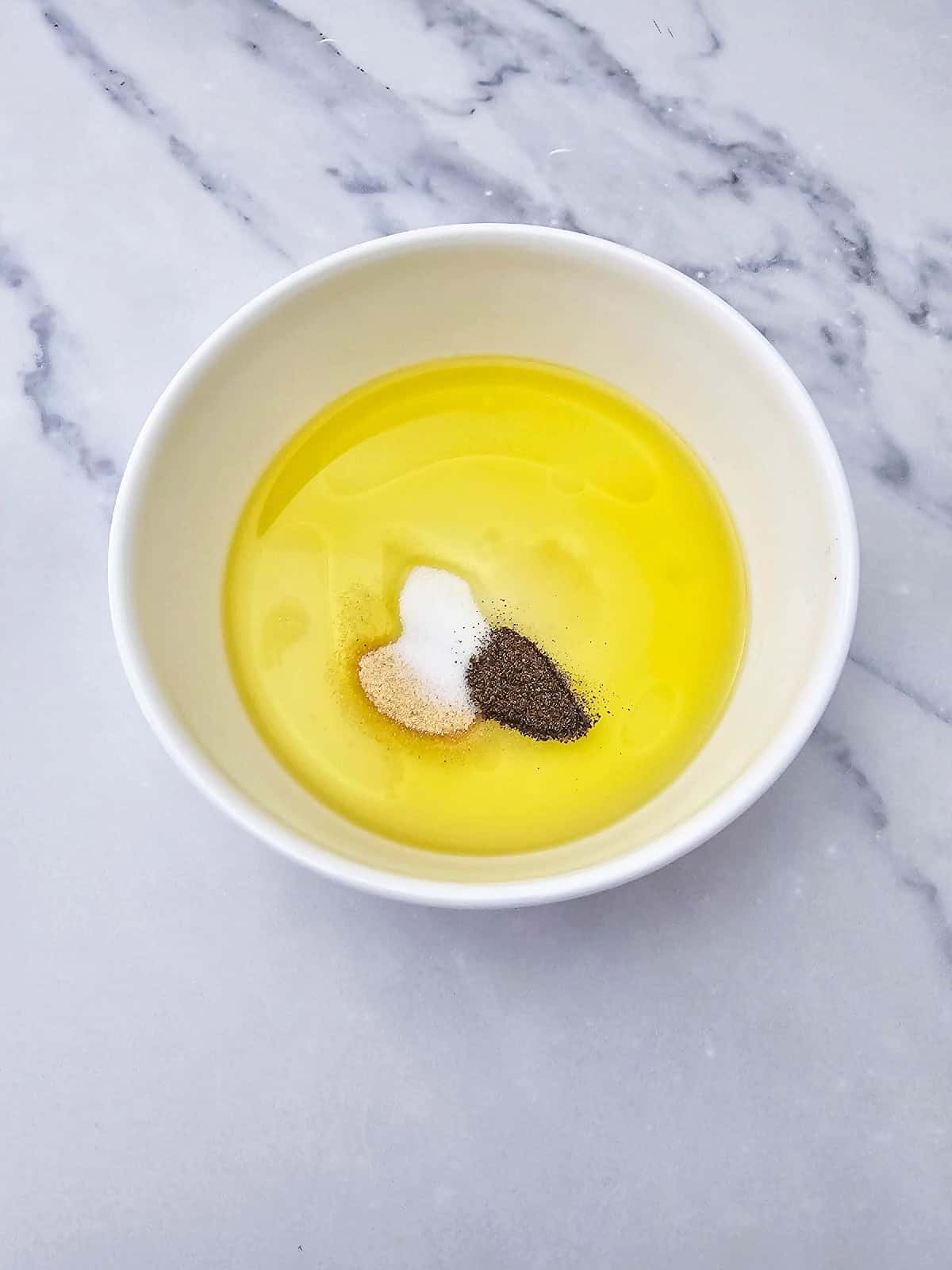 Olive oil, salt, black pepper, and garlic powder in a bowl for making vegan pasta salad dressing.
