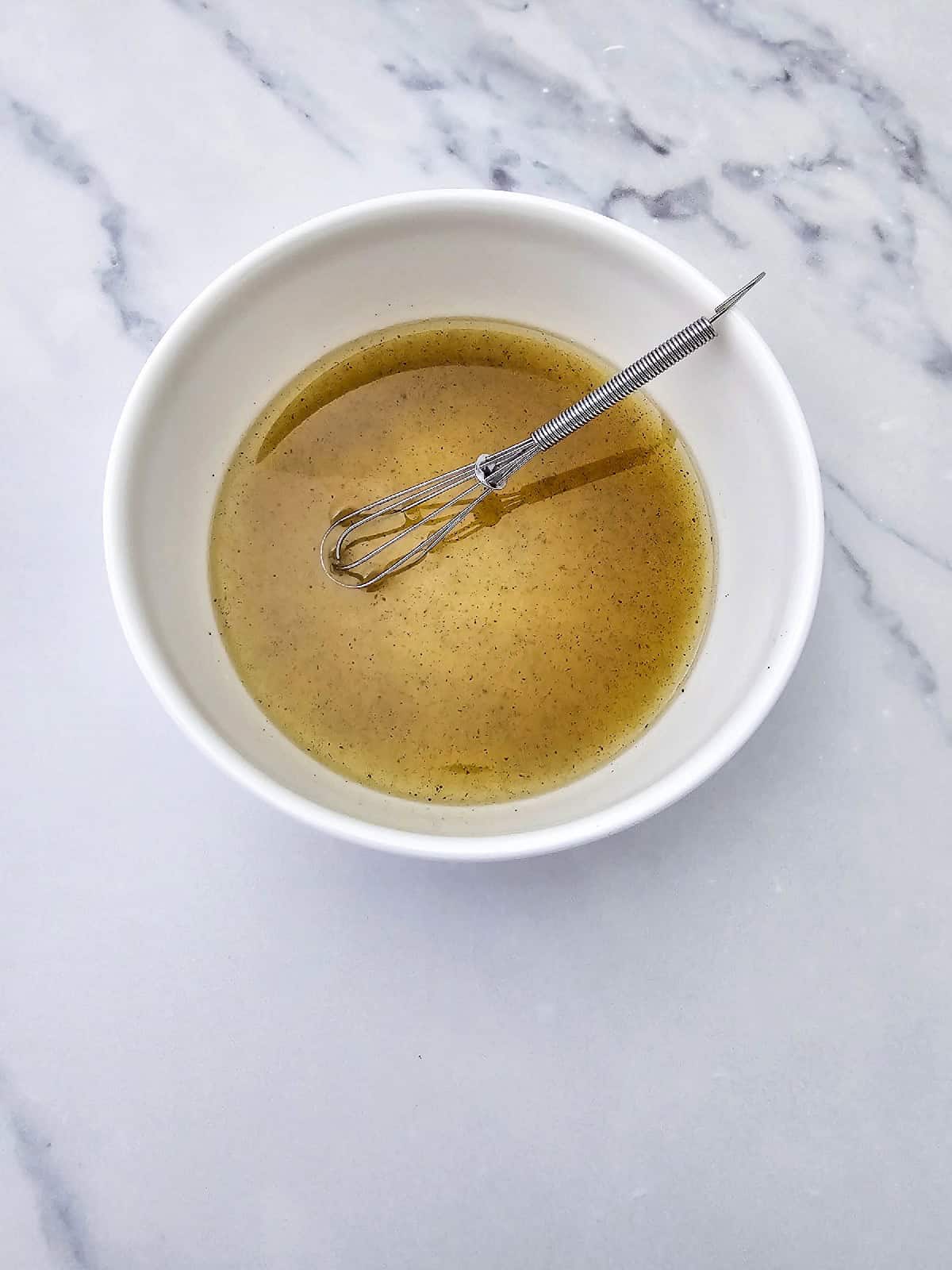 Homemade lemon olive oil dressing whisked together in a small white bowl.