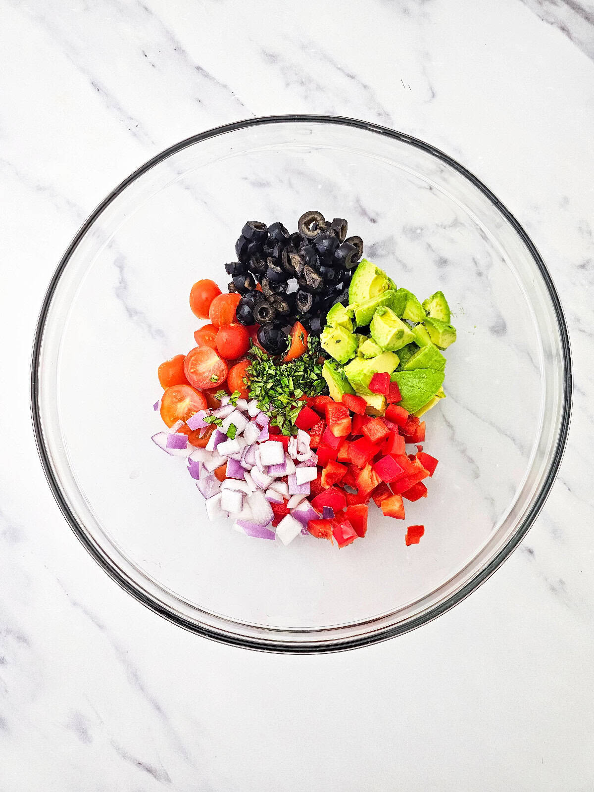 Avocado, cherry tomatoes, black olives, red bell pepper, red onion, and fresh basil combined in a large mixing bowl.