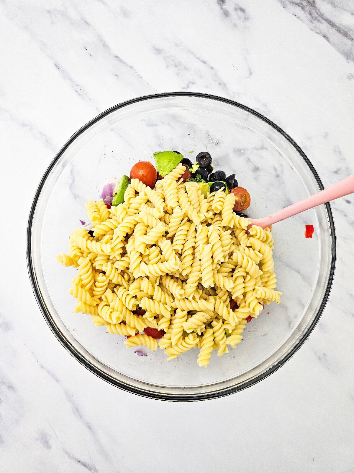 Cooked rotini pasta added to fresh vegetables in a large bowl before mixing.