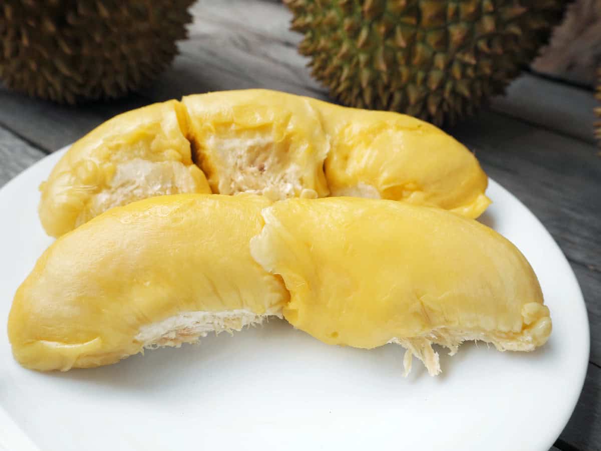 Creamy yellow durian flesh arranged on a white plate with whole durians in the background.
