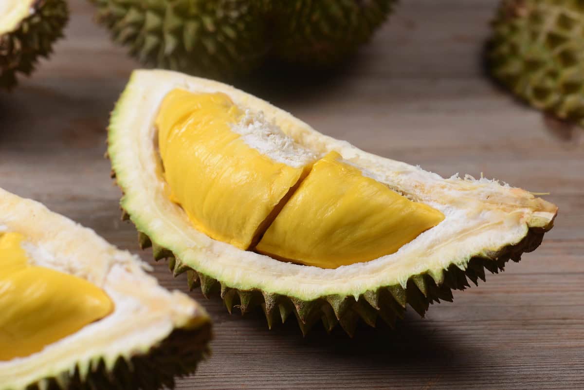 Ripe durian fruit cut open to reveal creamy yellow flesh inside the spiky shell.