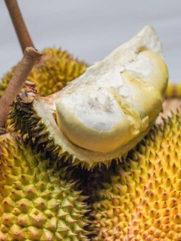Whole ripe durians with a cut section displaying pale creamy flesh and the spiky outer shell.