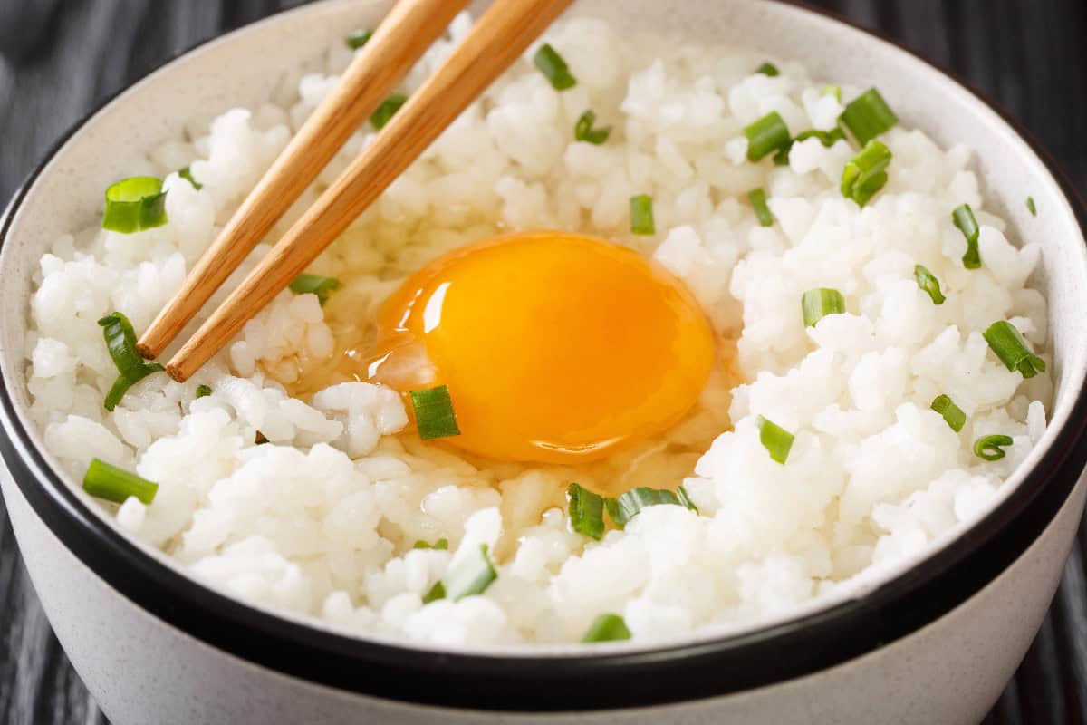 Raw egg served over steamed white rice with chopped green onions and chopsticks.
