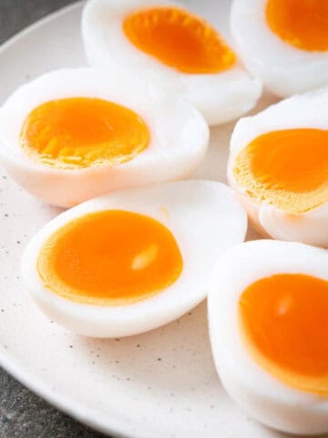 Soft-boiled eggs with bright orange yolks sliced in half and arranged on a white plate.