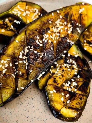 Close-up of roasted miso glazed eggplant halves topped with sesame seeds and caramelized miso sauce on a speckled plate.