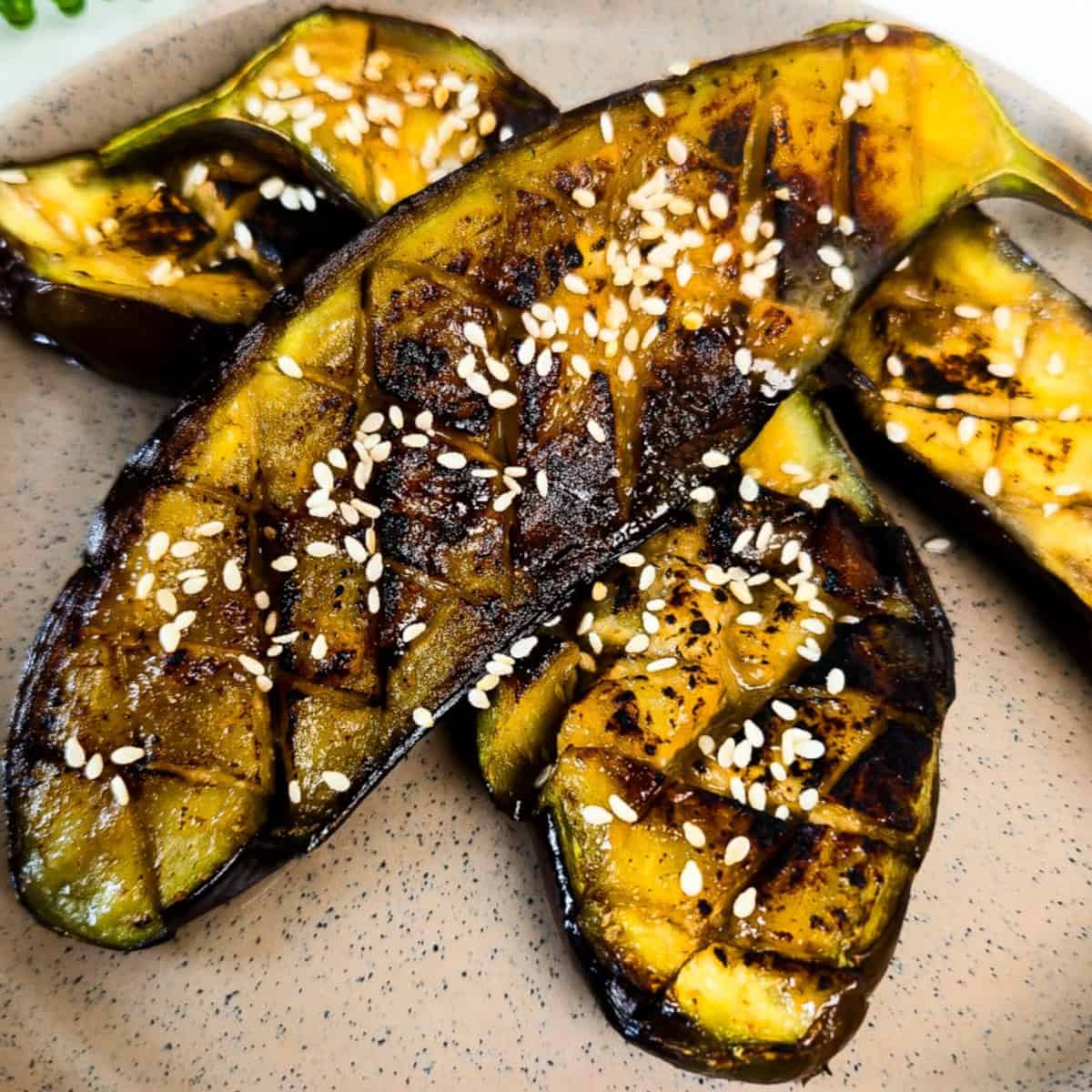 Close-up of roasted miso glazed eggplant halves topped with sesame seeds and caramelized miso sauce on a speckled plate.