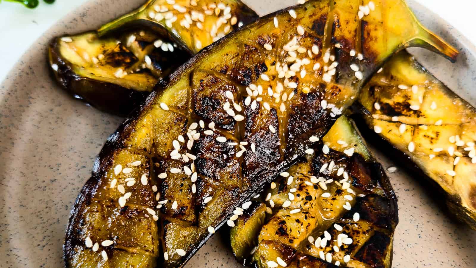 Close-up of roasted miso glazed eggplant halves topped with sesame seeds and caramelized miso sauce on a plate.
