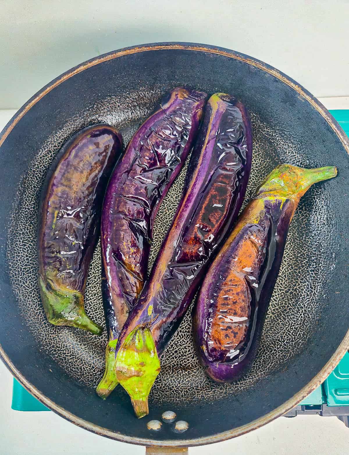 Whole Japanese eggplants cooking in a skillet until softened and glossy.