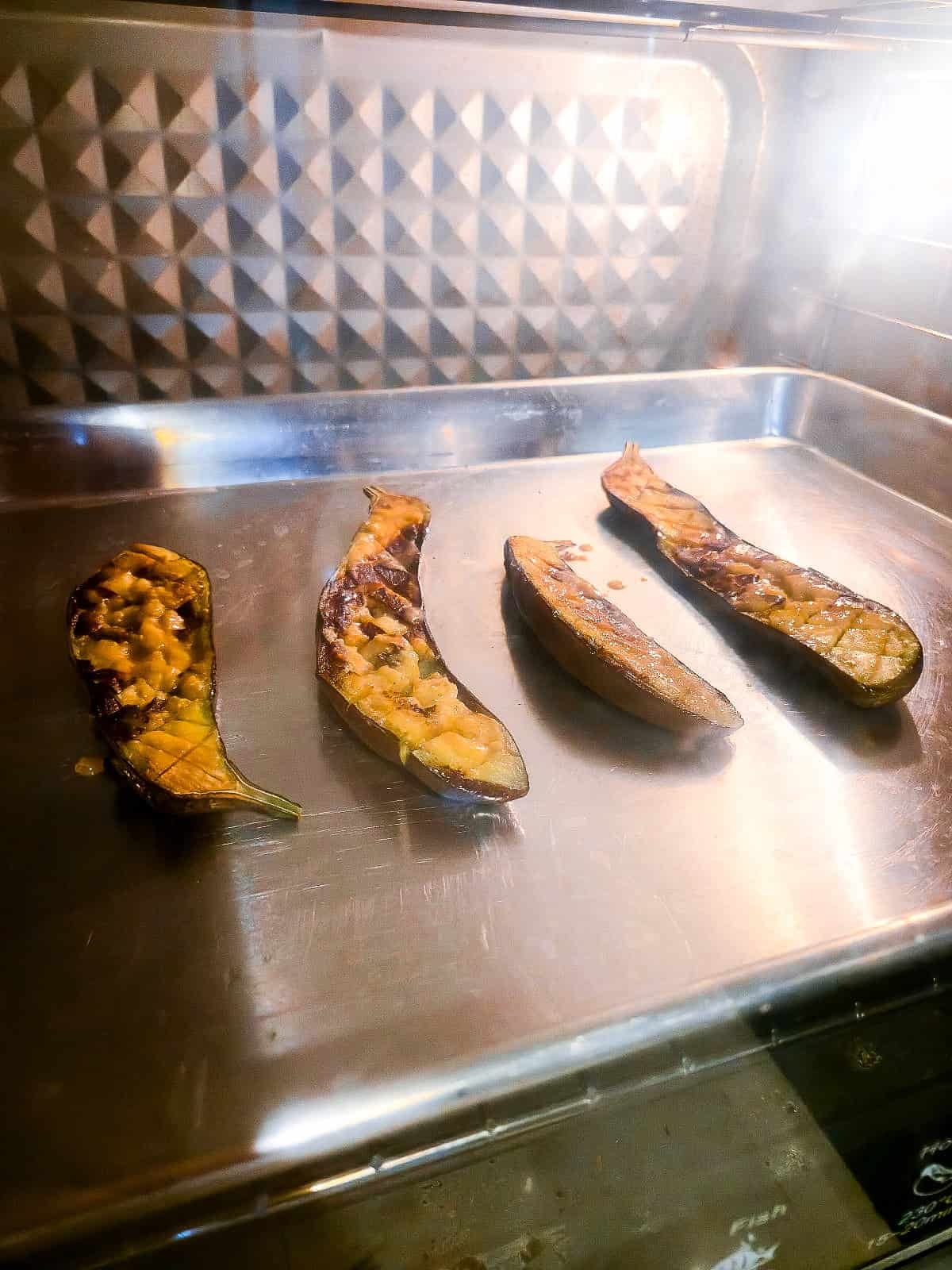 Eggplant halves roasting in the oven with miso glaze spread over the cut surface.