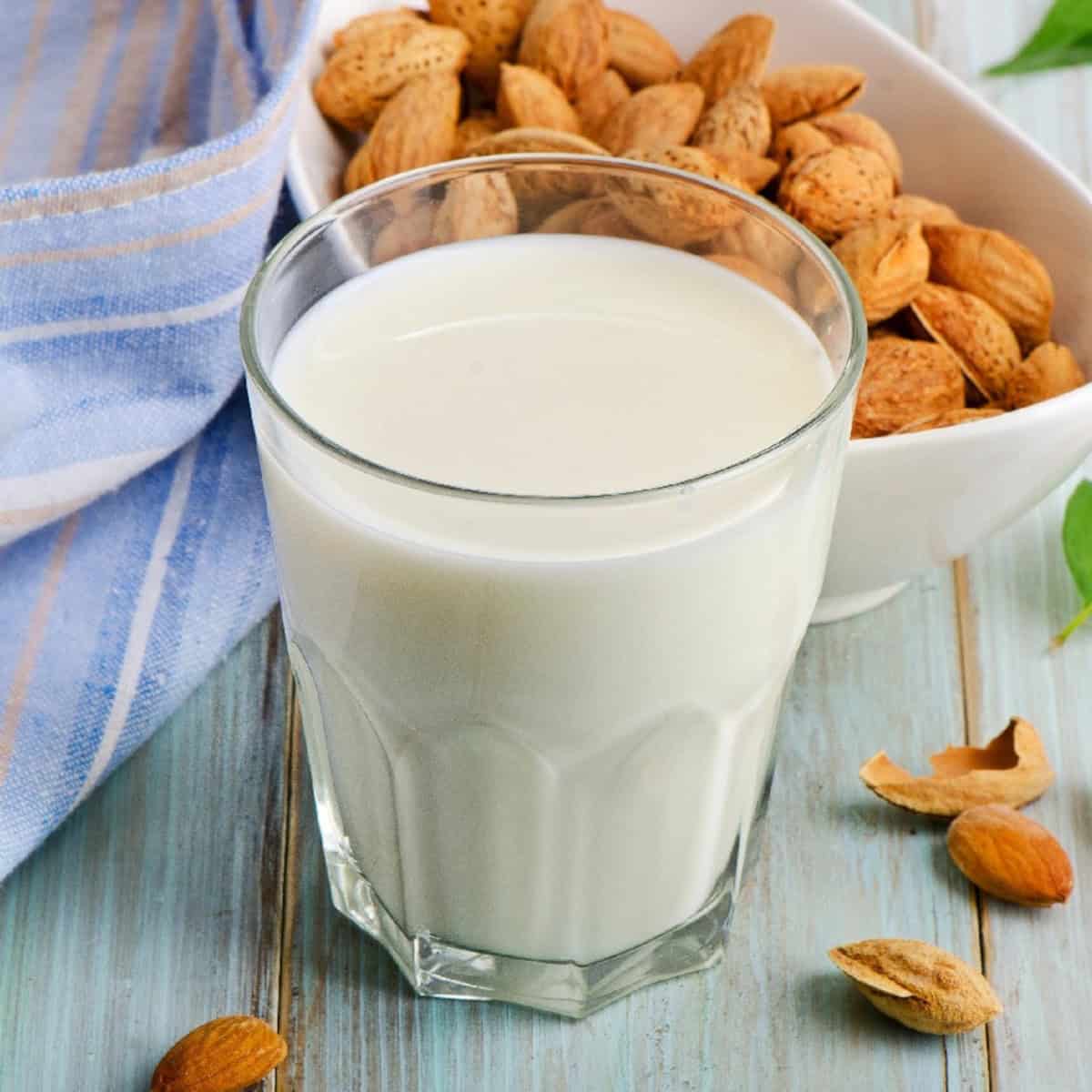 Glass of almond milk with almonds and green leaves on a blue wooden surface.
