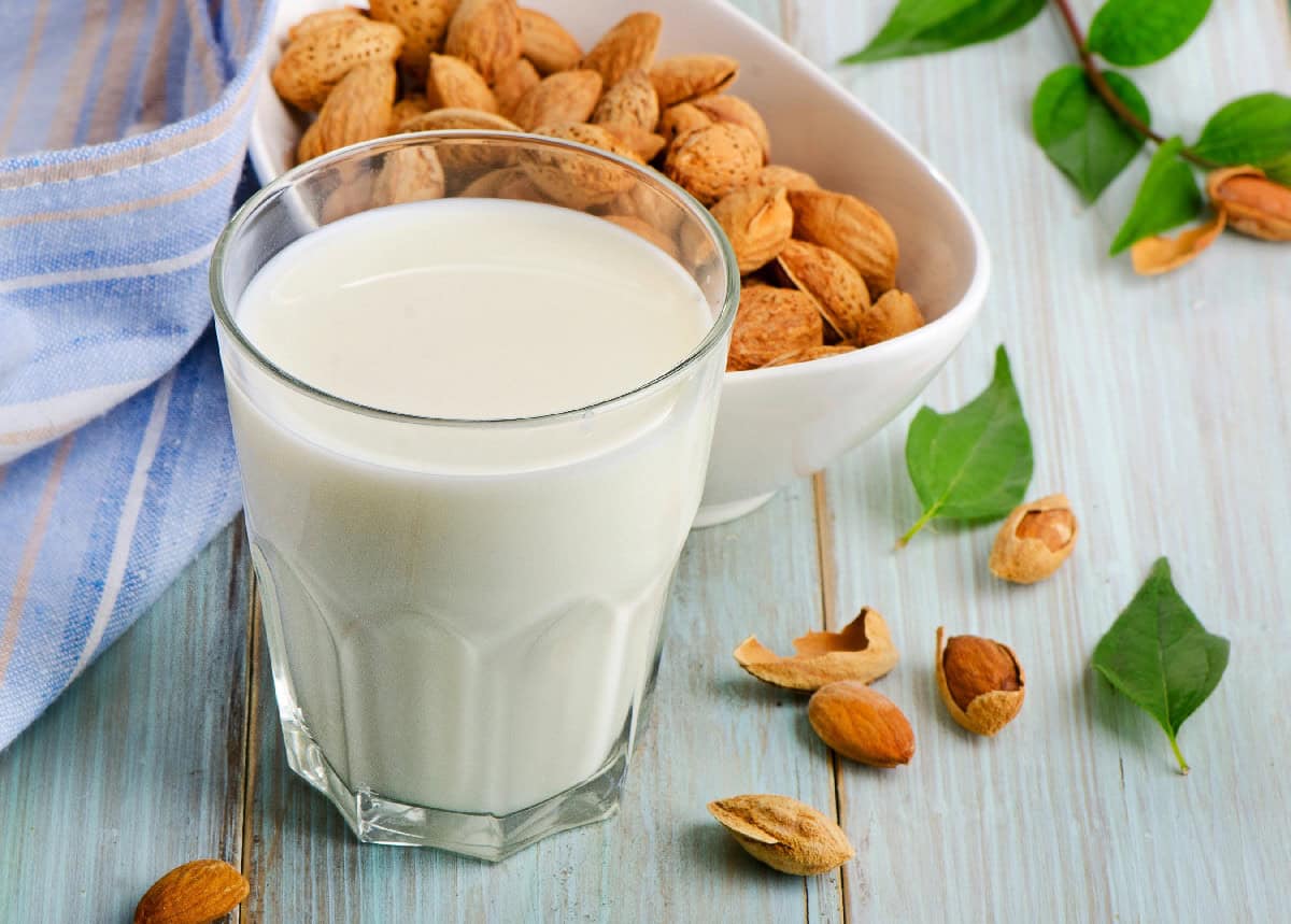 Glass of almond milk with almonds and green leaves on a rustic blue wooden surface.