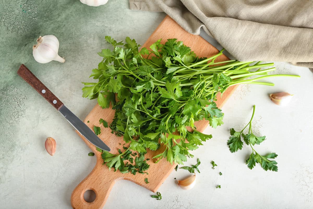 Fresh flat-leaf parsley on a wooden board with garlic cloves and a knife.