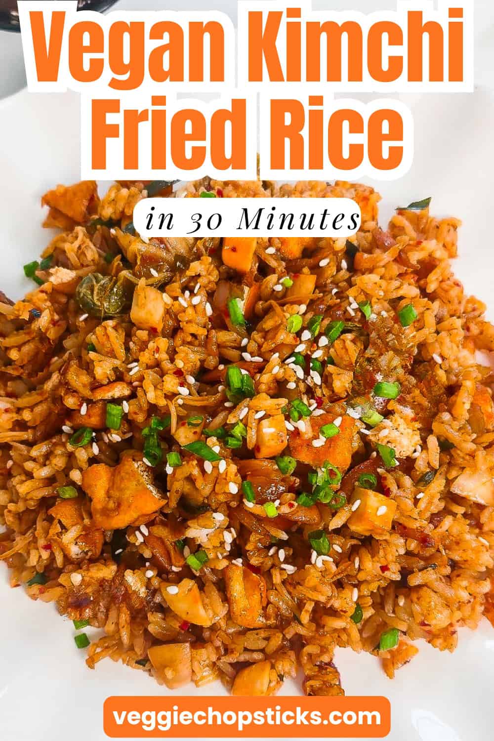 Close-up overhead view of vegan kimchi fried rice topped with sesame seeds and chopped green onions on a plate.