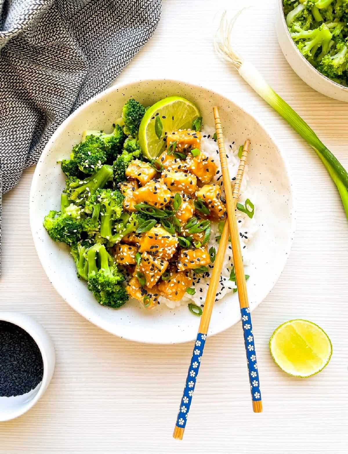 Sesame tofu and broccoli rice bowl served with chopsticks and fresh lime.