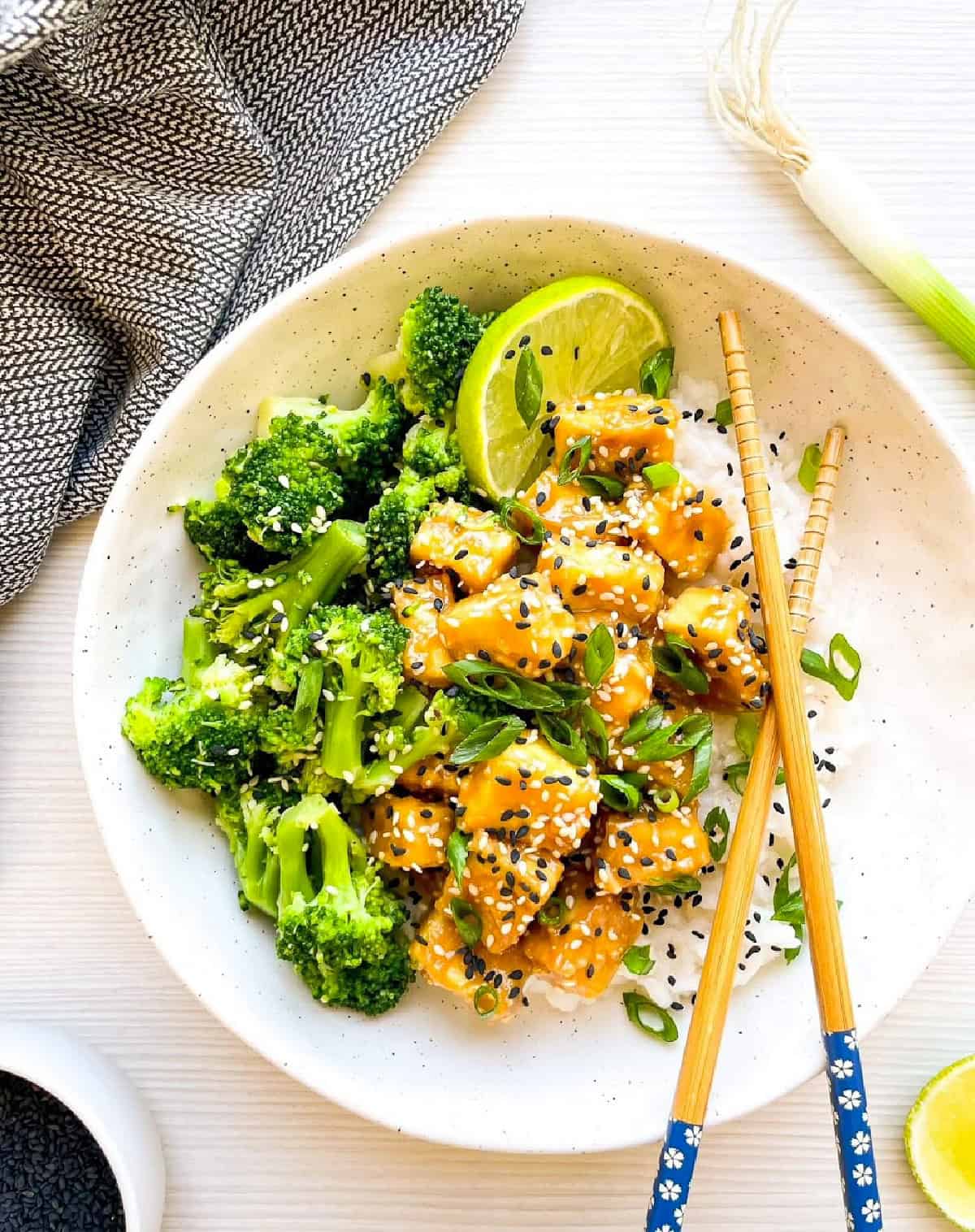 Close-up of sesame tofu with broccoli over white rice topped with scallions and sesame seeds.