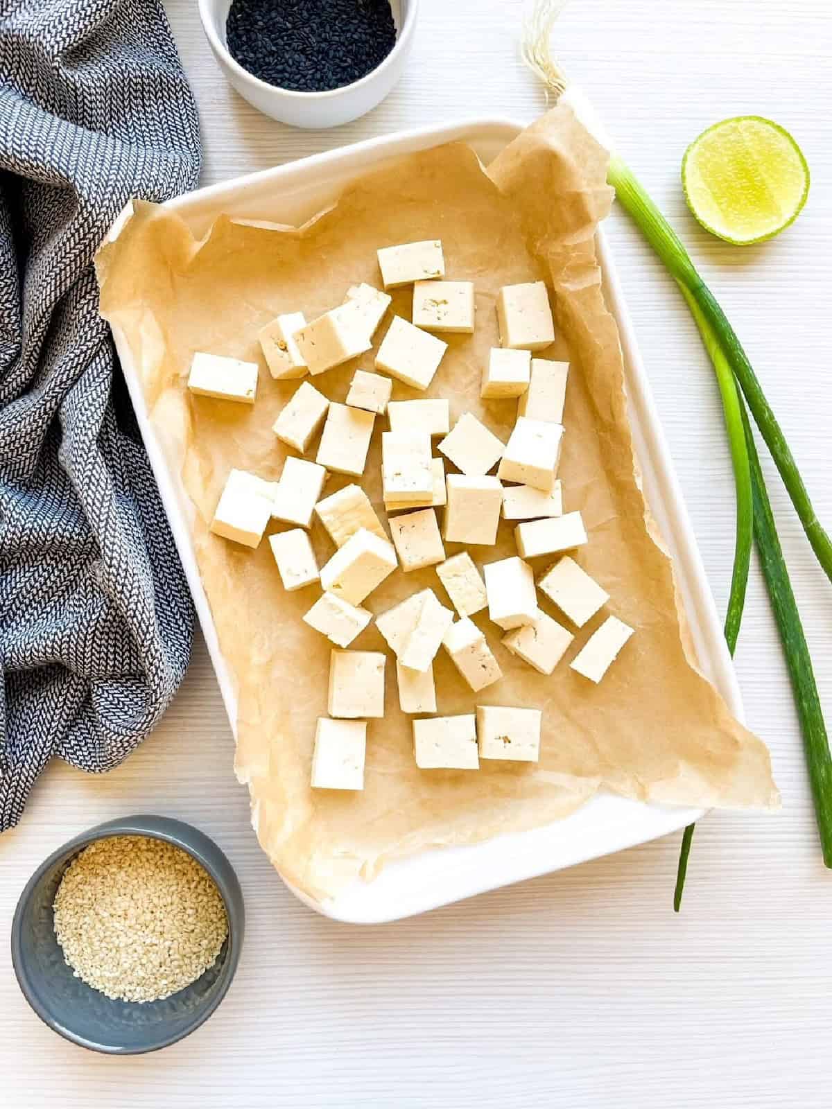 Cubed firm tofu arranged on a parchment-lined baking tray before seasoning.