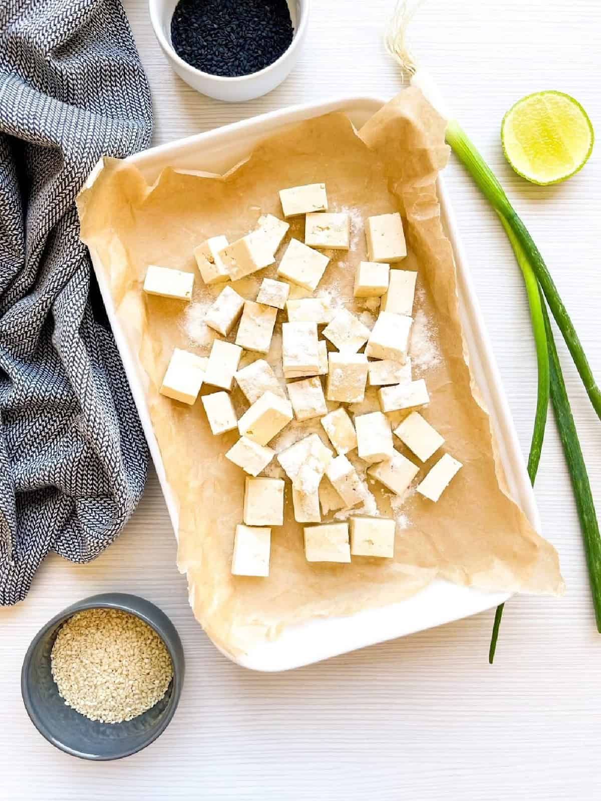 Firm tofu cubes coated with cornstarch on a baking tray before baking.