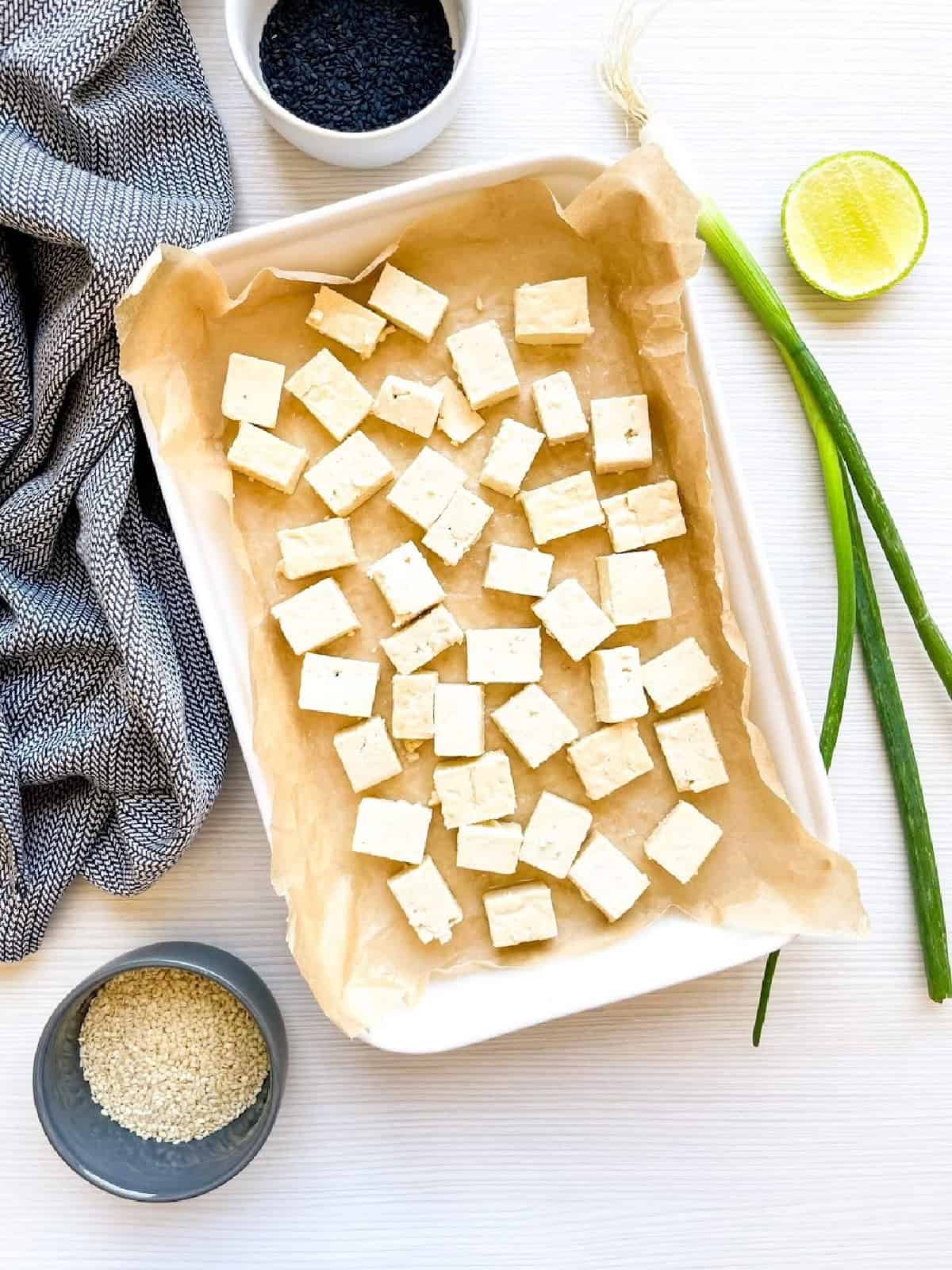 Cornstarch-coated tofu cubes spread evenly on a parchment-lined baking sheet.