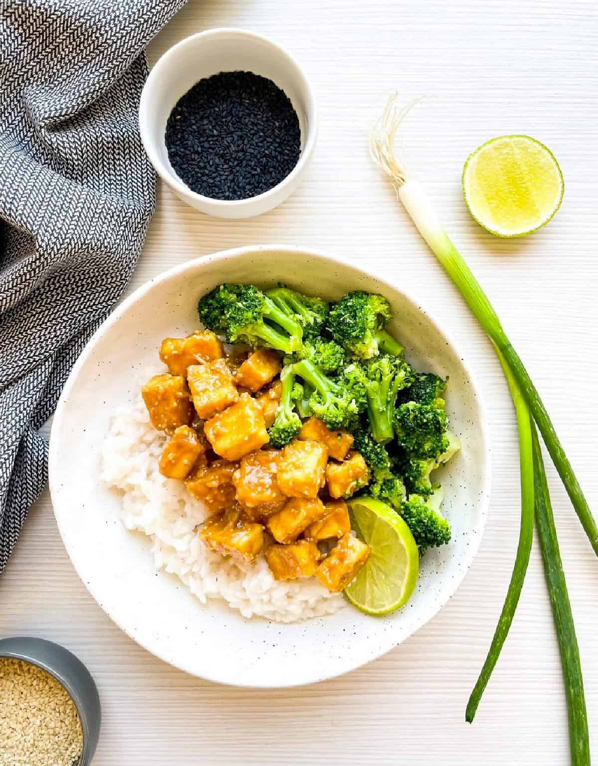 Sesame tofu with broccoli served over steamed rice with a lime wedge.