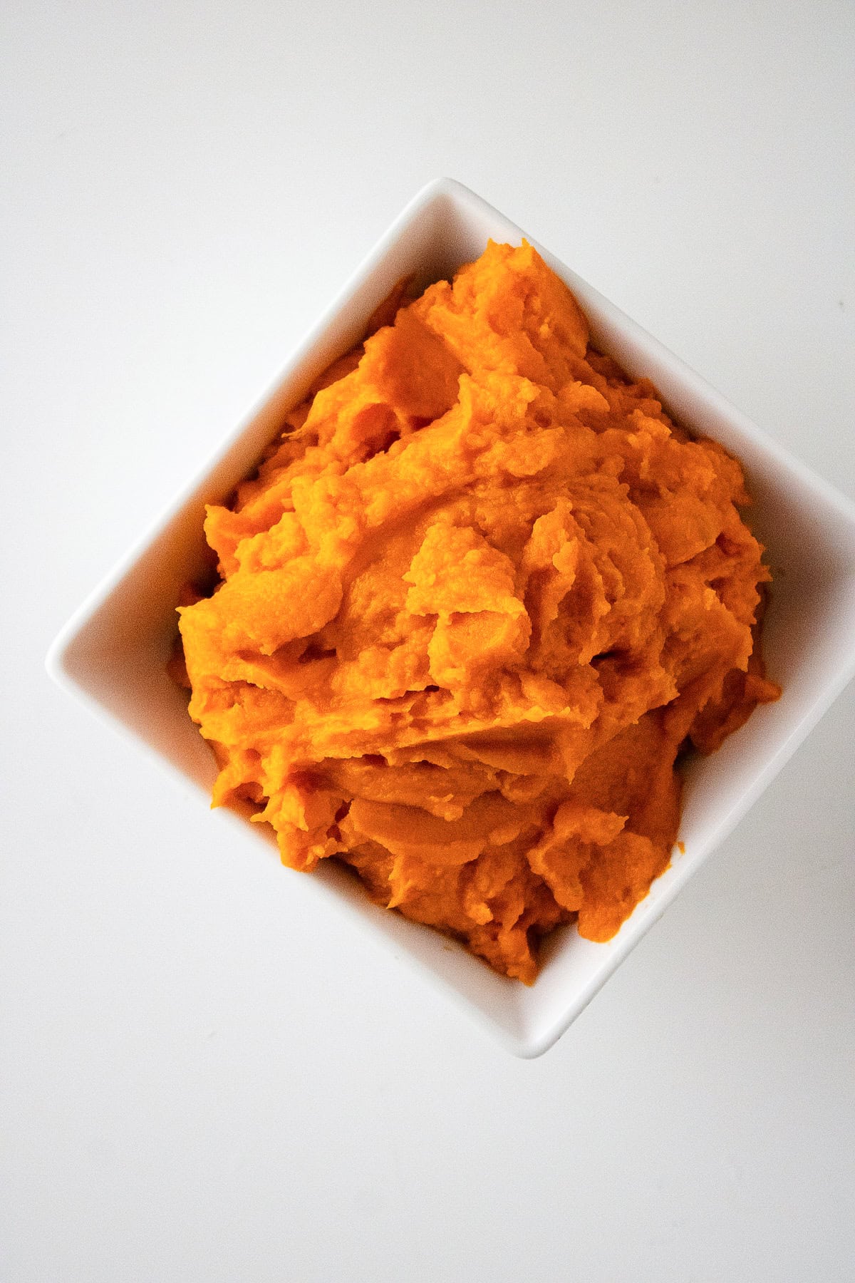 Homemade sweet potato puree in a white square bowl viewed from above on a white tabletop.