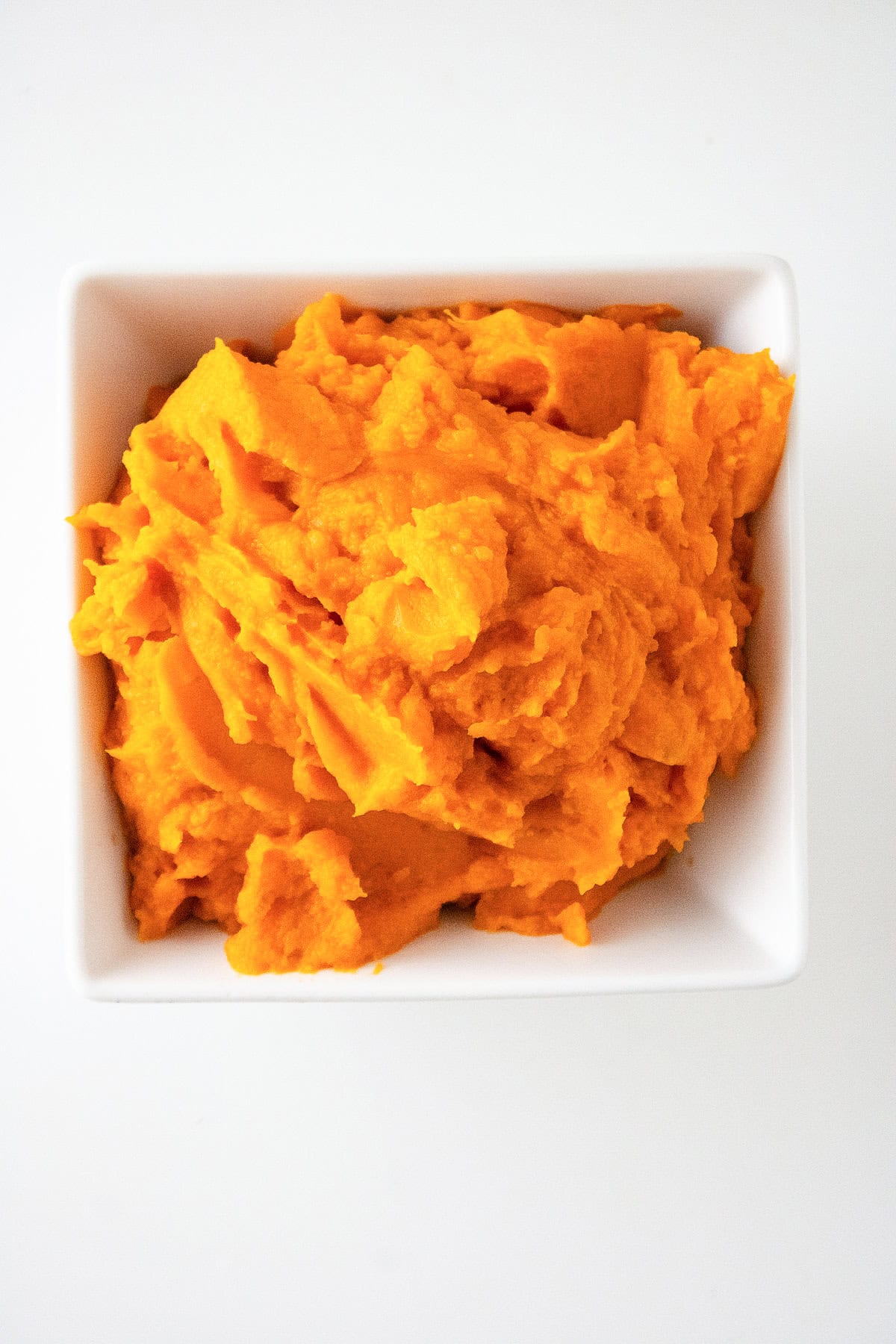Creamy mashed sweet potato puree in a white bowl with smooth texture and vibrant orange color.