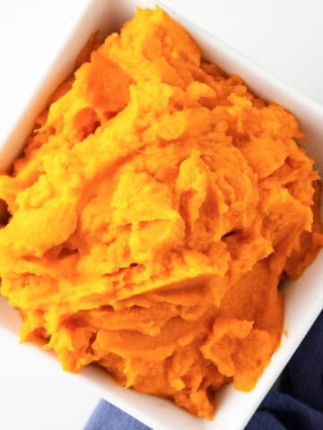 Overhead shot of sweet potato puree in a white bowl with a cloth napkin beside it.