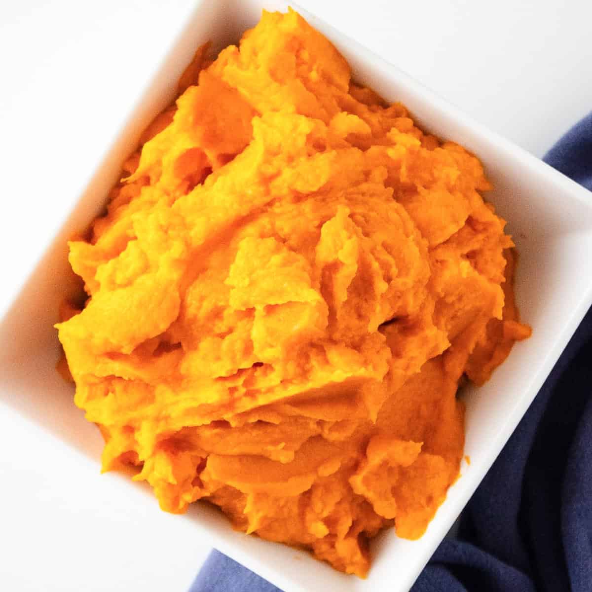 Overhead shot of sweet potato puree in a white bowl with a cloth napkin beside it.