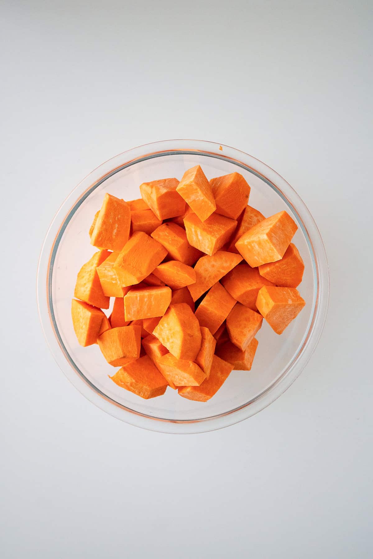 Peeled and cubed sweet potatoes in a clear glass bowl, ready for cooking.